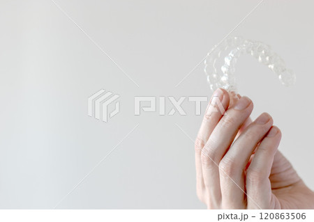 Hand holding Invisalign transparent braces on white background with copy space. Orthodontic invisible retainers and aligners 120863506