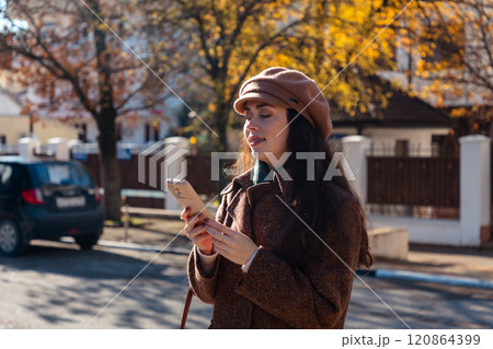 Portrait of a young Caucasian woman in a autumn coat and beret using smartphone on street. Modern communication and business 120864399