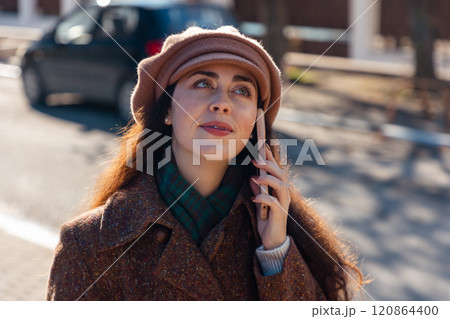 Portrait of a young Caucasian woman in a coat and beret, with braces on her teeth, talking on the street on a smartphone. Urban lifestyle Portrait of a young Caucasian woman in a coat and beret, with braces on her teeth, talking on the street on a smartphone. Urban lifestyle 120864400
