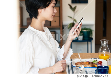 食事中にスマホを見る女性 120864733
