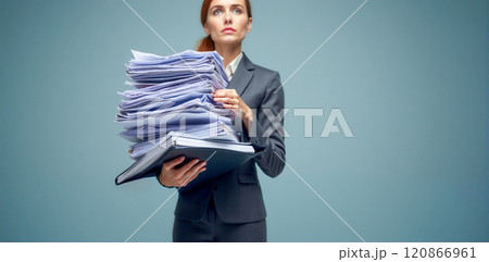 Overworked businesswoman in grey suit carrying large stack of documents and files, representing office stress, work overload, and corporate pressure in professional environment Overworked businesswoman in grey suit carrying large stack of documents and files, representing office stress, work overload, and corporate pressure in professional environment 120866961