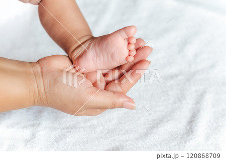 A baby's foot is held in a mother's hand. The baby is small and the mother is holding it gently. 120868709