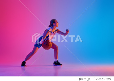 Dynamic image of young teen girl, basketball player in motion with ball, training, playing against gradient pink blue background in neon light Dynamic image of young teen girl, basketball player in motion with ball, training, playing against gradient pink blue background in neon light 120869869