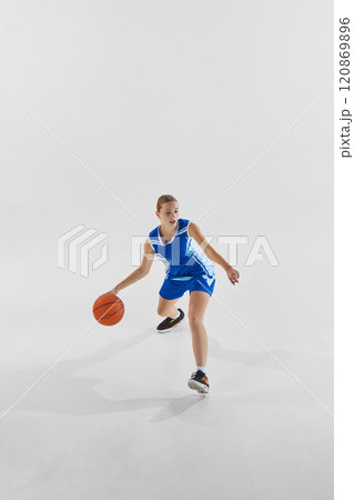 Focused teen girl, basketball player in blue uniform in motion with ball, training against white studio background. Dribbling. 120869896