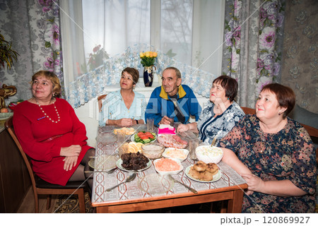 Family and senior friends eating together and watching tv show together at home 120869927