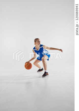 Dynamic image of teen girl in motion with ball, wearing blue uniform, competing for the victory, playing against white studio background 120869941