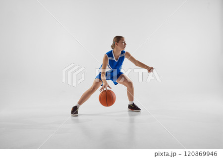 Competitive young girl, basketball player in blue uniform in motion with ball, training with motivation to win against white studio background Competitive young girl, basketball player in blue uniform in motion with ball, training with motivation to win against white studio background 120869946