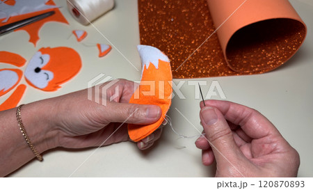 Woman sews on edges of fox toy tail using orange felt 120870893