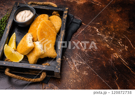 Crusted Fish sticks fingers with lemon and tartar sauce in wooden tray. brown background. top view Crusted Fish sticks fingers with lemon and tartar sauce in wooden tray. brown background. top view 120872738