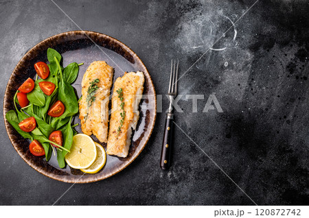 Roast Cod fish fiilets, white fish meat on plate with salad. Black background. top view 120872742