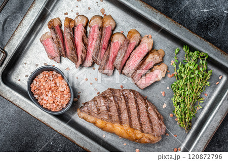 Grilled and sliced brazilian Picanha steak, cup rump beef meat steak on a steel serving tray with herbs. Black background. Top view. Copy space Grilled and sliced brazilian Picanha steak, cup rump beef meat steak on a steel serving tray with herbs. Black background. Top view. Copy space 120872796