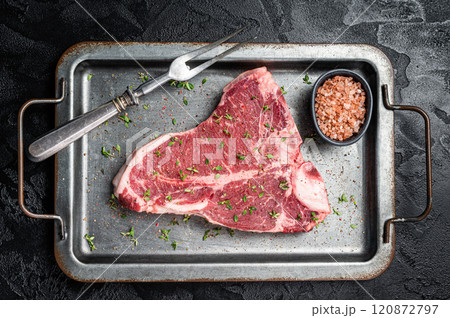 T-bone steak, raw marbled beef meat in a steel kitchen tray with herbs. Black background. Top view T-bone steak, raw marbled beef meat in a steel kitchen tray with herbs. Black background. Top view 120872797