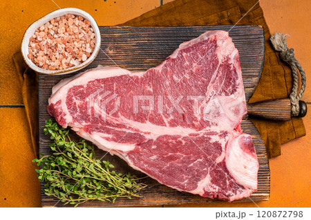 Porterhouse raw beef meat Steak, T-bone with thyme and sea salt on a wooden board. Orange background. Top view Porterhouse raw beef meat Steak, T-bone with thyme and sea salt on a wooden board. Orange background. Top view 120872798