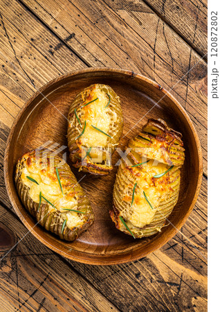 Hasselback potatoes with cheese, garlic and herbs. Wooden background. Top view 120872802