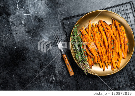 Baked sweet potato fries on a plate with herbs. Black background. Top view. Copy space 120872819