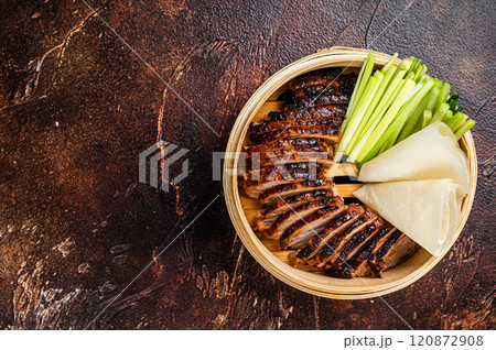 Peking Duck in bamboo steamer served with cucumber, green onion, and wheaten chinese pancakes. Dark background. Top view. Copy space 120872908