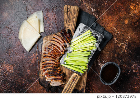 Sliced Peking Duck served with cucumber, green onion, and wheaten chinese pancakes on a meat cleaver. Dark background. Top view Sliced Peking Duck served with cucumber, green onion, and wheaten chinese pancakes on a meat cleaver. Dark background. Top view 120872978