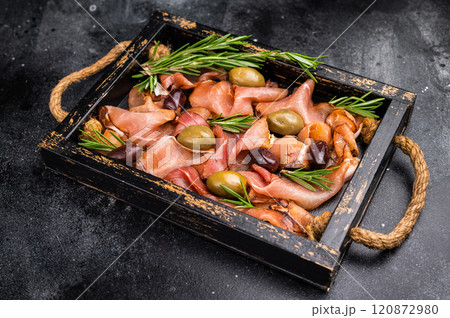 Prosciutto ham or Jamon Serrano with rosemary and olives in wooden tray. black background. top view 120872980