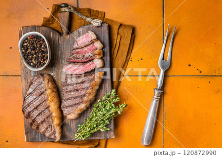 BBQ Roast brazilian Picanha steak, cup rump beef meat steak on a wooden serving board. Orange background. Top view 120872990