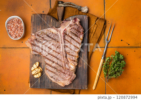 BBQ Roast T bone or Porterhouse beef meat Steak on a wooden board with spices. Orange background. Top view BBQ Roast T bone or Porterhouse beef meat Steak on a wooden board with spices. Orange background. Top view 120872994