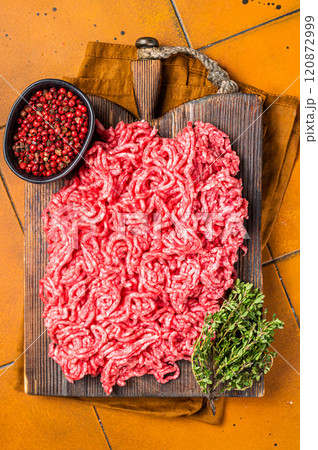 Fresh Raw Mince, Ground beef and pork meat on a butcher board. Orange background. Top view Fresh Raw Mince, Ground beef and pork meat on a butcher board. Orange background. Top view 120872999