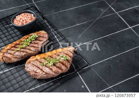 Grilled top sirloin or cup rump beef meat steak on a rack. Black background. Top view. Copy space 120873057