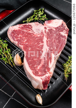 Raw T-bone or porterhouse beef meat Steak with thyme in a grill skillet ready for cooking. Black background. Top view 120873068