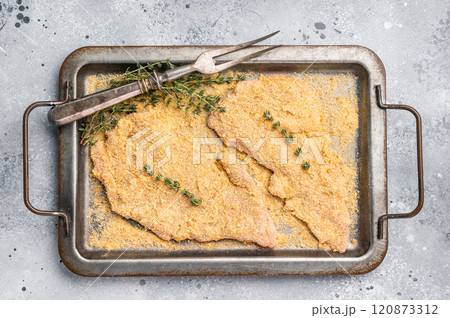 Cooking of Raw breaded Wiener Schnitzel steak in steel tray. gray background. top view Cooking of Raw breaded Wiener Schnitzel steak in steel tray. gray background. top view 120873312