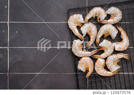 Raw shrimps, headless fresh prawns on a rack. Top view. Black background 120873576