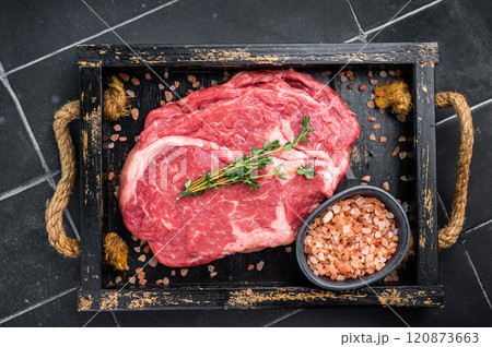 Marbled raw Rib eye steak with herbs in wooden tray, fresh beef meat. black kitchen background. top view Marbled raw Rib eye steak with herbs in wooden tray, fresh beef meat. black kitchen background. top view 120873663