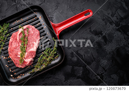 Raw Rib eye steak in a grill skillet with herbs, prime beef meat. black background. top view 120873670