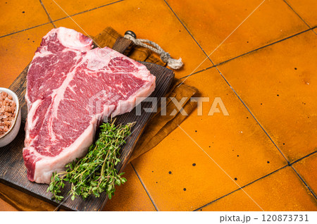 Porterhouse raw beef meat Steak, T-bone with thyme and sea salt on a wooden board. Orange background. Top view. Copy space Porterhouse raw beef meat Steak, T-bone with thyme and sea salt on a wooden board. Orange background. Top view. Copy space 120873731