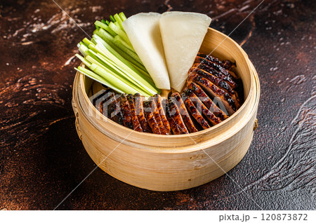Peking Duck in bamboo steamer served with cucumber, green onion, and wheaten chinese pancakes. Dark background. Top view 120873872