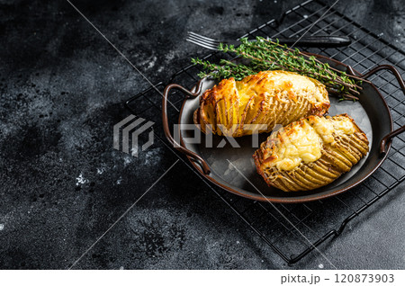 Baked hasselback potatoes with cheese, garlic, thyme and rosemary. Black background. Top view. Copy space 120873903
