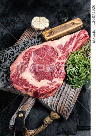 Dry aged Tomahawk rib eye steak, raw beef meat on butcher table. Black background. Top view Dry aged Tomahawk rib eye steak, raw beef meat on butcher table. Black background. Top view 120873926