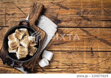 Toasted Marshmallow on open campfire in a skillet. Wooden background. Top view. Copy space 120873929