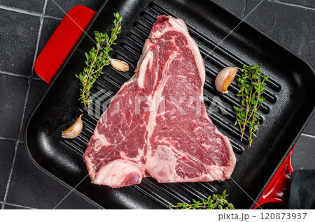 Raw T-bone or porterhouse beef meat Steak with thyme in a grill skillet ready for cooking. Black background. Top view Raw T-bone or porterhouse beef meat Steak with thyme in a grill skillet ready for cooking. Black background. Top view 120873937
