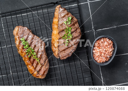 Grilled top sirloin or cup rump beef meat steak on a rack. Black background. Top view 120874088