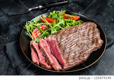 Grilled medium rare flank beef steak with salad in a plate. Black background. Top view Grilled medium rare flank beef steak with salad in a plate. Black background. Top view 120874140