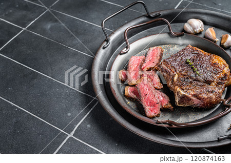 Roasted Sliced Wagyu New York beef meat steak or Striploin steak in a steel tray with herbs. Black background. Top view. Copy space 120874163
