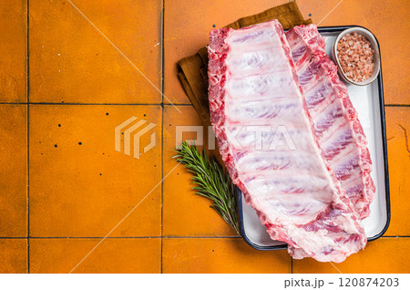 Fresh Raw pork spare loin ribs in a steel tray with herbs. Orange background. Top view. Copy space Fresh Raw pork spare loin ribs in a steel tray with herbs. Orange background. Top view. Copy space 120874203