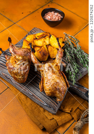 Roasted quails with potatoes, spices and herbs on a wooden board. Orange background. Top view 120874262