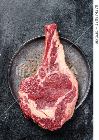 Raw cowboy steak, rib eye steak with bone, beef marbled meat on butcher cutting board. Black background. Top view Raw cowboy steak, rib eye steak with bone, beef marbled meat on butcher cutting board. Black background. Top view 120874279