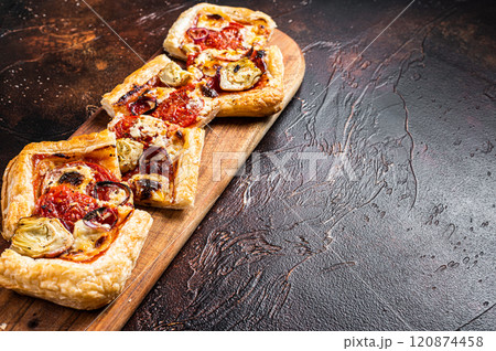 Baked Puff pastry tart pizza with artichoke, mozzarella, tomatoes and cheese sliced on a wooden board. Dark background. Top view. Copy space Baked Puff pastry tart pizza with artichoke, mozzarella, tomatoes and cheese sliced on a wooden board. Dark background. Top view. Copy space 120874458