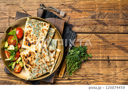 Gozleme flatbread with greens and vegetable salad on garnish. Wooden background. Top view. Copy space Gozleme flatbread with greens and vegetable salad on garnish. Wooden background. Top view. Copy space 120874459