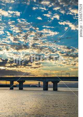 美しい夕日に照らされた海とセントレア大橋を渡る名鉄空港線の縦構図風景(愛知県) 120877029
