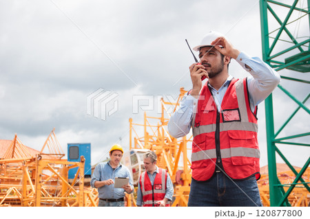 Worker at construction site, communicating with colleague on walkie Talkie. Worker at construction site, communicating with colleague on walkie Talkie. 120877800