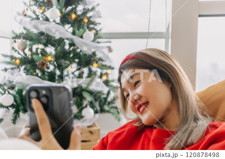 Happy red shirt woman making a video call holiday greeting with her friends and family showing the Christmas tree. Happy red shirt woman making a video call holiday greeting with her friends and family showing the Christmas tree. 120878498