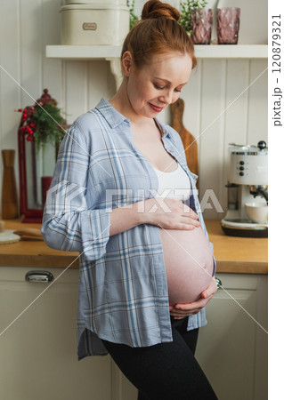 Pregnancy motherhood people expectation future. Pregnant woman with big belly smiling in kitchen at home. Girl hugging her tummy enjoying pregnancy. Maternity tenderness parenthood new life concept 120879321