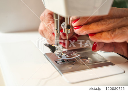Hands of an older woman threading the sewing machine needle before starting. 120880723